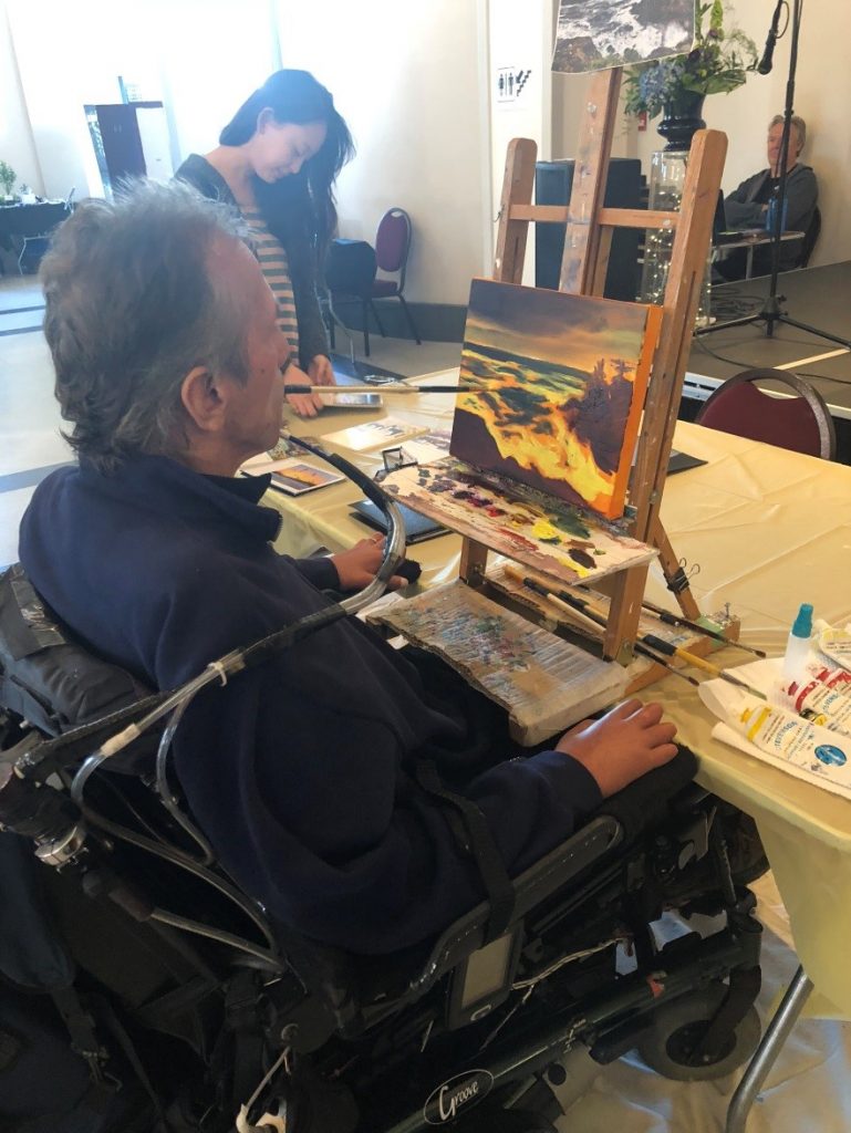 A man in a wheelchair painting with his mouth. 