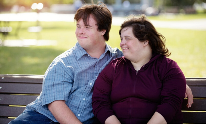A man and woman with disabilities sitting together on a park bench.
