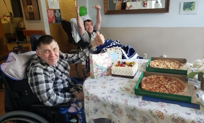 Two men in a group home celebrate with cake and pizza
