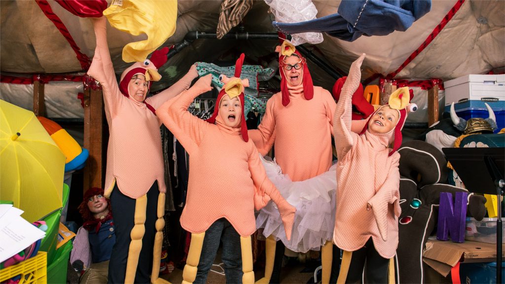 Two adults and two children in chicken costumes strike a hilarious pose among the assorted props and costumes from previous East Van Pantos
