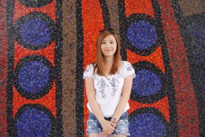 Asian woman with orange hair smiling in front of a red, blue and brown mural.