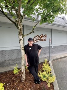 A man stands by a small tree in front of a McCafe sign