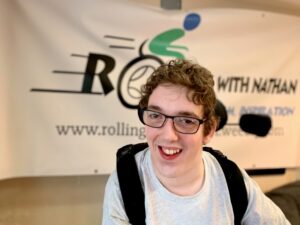 Nathan Shipley, a smiling young man in a wheelchair., wearing glasses 